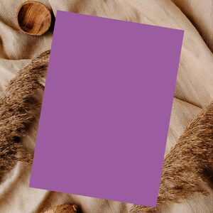 Op de afbeelding: Een platte lay-out met een effen paarse rechthoekige kaart, een kleine houten kom en gedroogd siergras. De items zijn gerangschikt op een beige, getextureerde stof, waardoor een neutrale en natuurlijke esthetiek ontstaat.