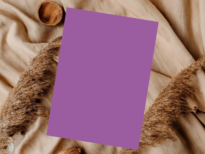 Op de afbeelding: Een platte lay-out met een effen paarse rechthoekige kaart, een kleine houten kom en gedroogd siergras. De items zijn gerangschikt op een beige, getextureerde stof, waardoor een neutrale en natuurlijke esthetiek ontstaat.