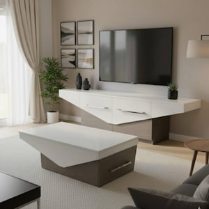May include: Contemporary living room with a white and grey TV unit and matching coffee table. The TV unit has drawers with silver handles. The coffee table has an angled design. The room is decorated in neutral tones and includes a potted plant.