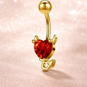 Può includere: Anello per ombelico color oro con un design a cuore diabolico. Il cuore è una gemma rossa sfaccettata e l'anello presenta piccole corna e una coda. La sfera superiore e la barra curva sono anch'esse color oro.
