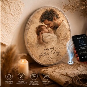 May include: A round, textured mulberry paper plaque featuring a sepia-toned photograph of a person holding a baby, with the text "happy father's day" and a heart icon. An NFC-enabled smartphone displays a connection screen to play audio.