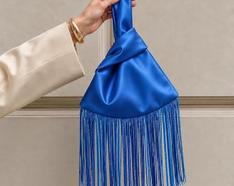 Peut inclure: Un sac à main en satin bleu roi vif doté d'une poignée supérieure nouée et d'une longue frange fluide qui s'étend depuis la base du sac. Le tissu lisse et lustré crée une apparence élégante avec une fermeture nouée très distincte.
