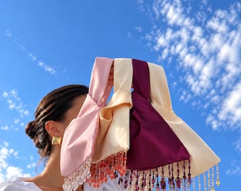 May include: A collection of four satin knot-handle bags in shades of light pink, cream, deep magenta, and beige. Each bag features a distinct fringe of hanging beads and crystals in coordinating colors along the bottom edge.