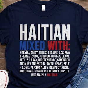 May include: Navy blue t-shirt with white and red text that reads "HAITIAN MIXED WITH:" followed by a list of words. The shirt is paired with blue jeans and white sneakers, suggesting casual wear.