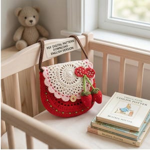 Peut inclure: Un sac à main crocheté rouge et crème avec une décoration de cerise. Le sac a une bandoulière marron et une fermeture à bouton. Le texte "PDF DIGITAL PATTERN - DOWNLOAD - ENGLISH VERSION" est visible. Un ours en peluche et des livres sont en arrière-plan.