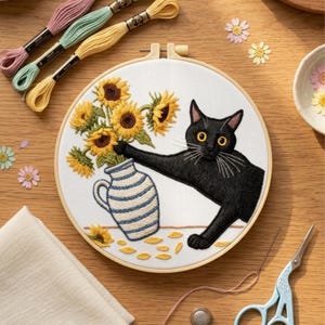 Könnte beinhalten: Gesticktes Stickrahmen-Kunstwerk mit einer schwarzen Katze, die nach Sonnenblumen in einer blau-weiß gestreiften Vase greift. Das Kunstwerk befindet sich auf weißem Stoff, umgeben von einem Holzrahmen. Stickgarn in Rosa, Grün und Gelb.