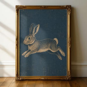 May include: A rectangular wall art print featuring a detailed, light-colored illustration of a rabbit in a leaping position against a dark blue, textured background. The artwork is enclosed in an ornate, metallic gold-toned decorative frame.