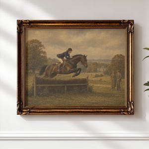 May include: A framed oil painting depicting a rider on a brown horse jumping over a wooden fence in a grassy field. Two figures stand in the background under a cloudy sky. The artwork is enclosed in an ornate, dark gold-toned rectangular frame.