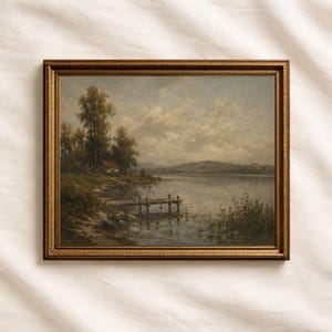 May include: A framed landscape painting depicts a serene lake scene. The artwork features a small house, trees, and a wooden dock. The color palette includes muted greens, blues, and browns, with a gold-colored frame.