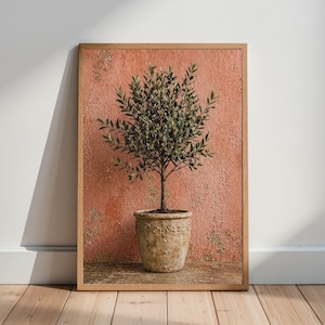 Könnte beinhalten: Gerahmter Kunstdruck eines Olivenbaums in einem dekorativen Topf. Der Baum hat grüne Blätter und kleine schwarze Oliven. Der Topf ist hellbraun mit einem detaillierten Design. Der Hintergrund ist eine strukturierte, rot-orange Wand.