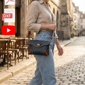 Könnte beinhalten: Eine blaue Leder-Umhängetasche mit braunen Wildlederakzenten und einem goldfarbenen Verschluss. Die Tasche wird über der Schulter getragen und hat einen braunen Lederriemen. Die rechteckige Tasche scheint handgefertigt zu sein.