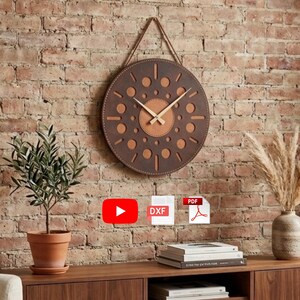 May include: A round, brown leather clock with a light brown center and wooden hands hangs on a brick wall. The clock features decorative cut-out circles. A small potted plant and a vase with dried flowers are on a wooden cabinet below.