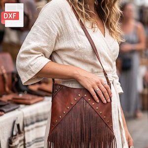 May include: A brown leather crossbody bag featuring a V-shaped front panel adorned with metallic studs and long fringe detailing. The bag includes a thin leather shoulder strap and a smooth, dark brown finish with visible grain texture throughout.