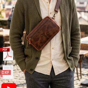 May include: A brown leather crossbody bag with a zipper closure and adjustable strap. The bag is worn over a green cardigan and a cream-colored button-down shirt. The bag's dimensions are approximately 10 inches long, 6 inches high, and 3 inches wide.