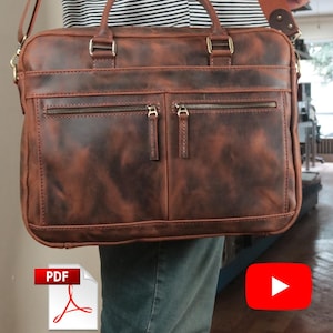 Puede incluir: Un maletín de cuero marrón con dos bolsillos delanteros con cremallera, dos asas superiores y una correa de hombro desmontable. El bolso tiene una forma rectangular con costuras visibles y herrajes metálicos, ofreciendo un diseño estructurado.
