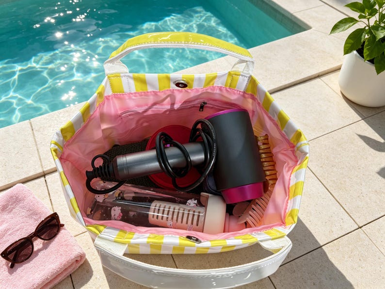 May include: A yellow and white striped tote bag with a pink interior lining. The bag contains a black and magenta hair dryer, a clear water bottle with a white filter insert, and a light-colored hair brush. The bag features white handles.