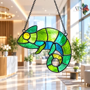 Pode incluir: Um apanhador de sol de vitral em forma de camaleão com segmentos de vidro texturizado verde, azul e amarelo unidos por perfis de metal preto. A peça pende de uma corrente de metal preto e inclui o logótipo ATS GLASS-PATTERN.