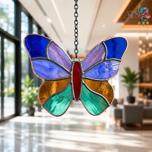 May include: A stained glass butterfly suncatcher featuring a red central body and wings composed of blue, purple, orange, and green glass segments held together by dark metal soldering. The butterfly hangs from a black metal chain.