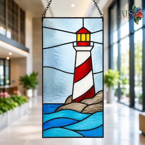 Op de afbeelding: Een rechthoekig glas-in-loodpaneel met een vuurtoren met rode en witte diagonale strepen, een gele lantaarnkamer en een rood dak. De vuurtoren staat op bruine rotsen boven blauwe golven tegen een lichtblauwe lucht, opgehangen aan een zwarte ketting.