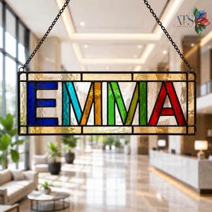 May include: A rectangular stained glass hanging sign featuring the name EMMA in bold, multi-colored block letters. Each letter is encased in a dark metal frame with textured glass panels in blue, teal, orange, green, and red hues.