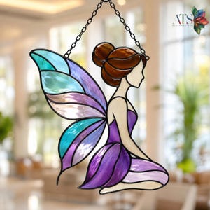 May include: A stained glass suncatcher depicting a figure with brown hair in a bun, wearing a purple dress, and featuring large wings with translucent panels of teal, light blue, and purple glass, suspended by a black metal chain.