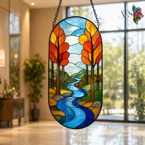 May include: An oval stained glass panel depicting a landscape scene. The artwork features a winding blue river, trees with orange and red leaves, and a blue sky. The panel is suspended by a black chain, showcasing a nature-themed design.