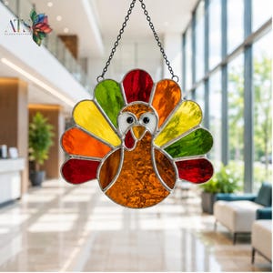 May include: A stained glass turkey suncatcher featuring a fan of colorful feathers in red, orange, yellow, and green. The turkey has a textured amber body, a white face with black eyes, and a red wattle, suspended by a black metal chain.