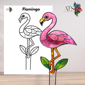 Puede incluir: Una escultura de flamenco de vidrieras con cuerpo rosa y magenta, pico amarillo y patas naranjas. La escultura está montada sobre una estaca de metal con hojas verdes. Un dibujo lineal en blanco y negro del flamenco está al lado, con la palabra "Flamingo" encima.
