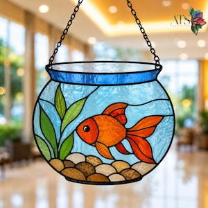 May include: Stained glass suncatcher depicting a goldfish in a bowl. The bowl is blue and clear with an orange fish, green plants, and brown stones. The suncatcher hangs from a black chain.
