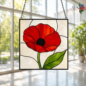 Op de afbeelding: Gebrandschilderd glaspaneel met een levendige rode klaproos met een zwart centrum en groen blad. Het kunstwerk is geplaatst tegen een crèmekleurige achtergrond en omlijst in zwart. Het hangt aan een ketting.