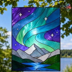 Op de afbeelding: Gebrandschilderd glaspaneel met een aurora borealis-sc&egrave;ne. Het kunstwerk toont wervelende blauwe, groene en paarse kleuren, met witte sterren en een bergketen aan de onderkant. Het paneel is zwart omlijst en hangt aan een ketting.