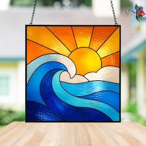 Può includere: Pannello in vetro colorato raffigurante una vivace scena oceanica. Un grande sole giallo irradia sopra un'onda blu e bianca. L'opera d'arte è incorniciata in nero e appesa a una catena. I colori includono sfumature di blu, arancione, giallo e bianco.