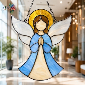 Può includere: Un acchiappasole in vetro colorato a forma di angelo con ali bianche, una veste blu e un pannello centrale color crema. La figura presenta un'aureola dorata dietro la testa ed è appesa a una catena di metallo nero con giunture scure.