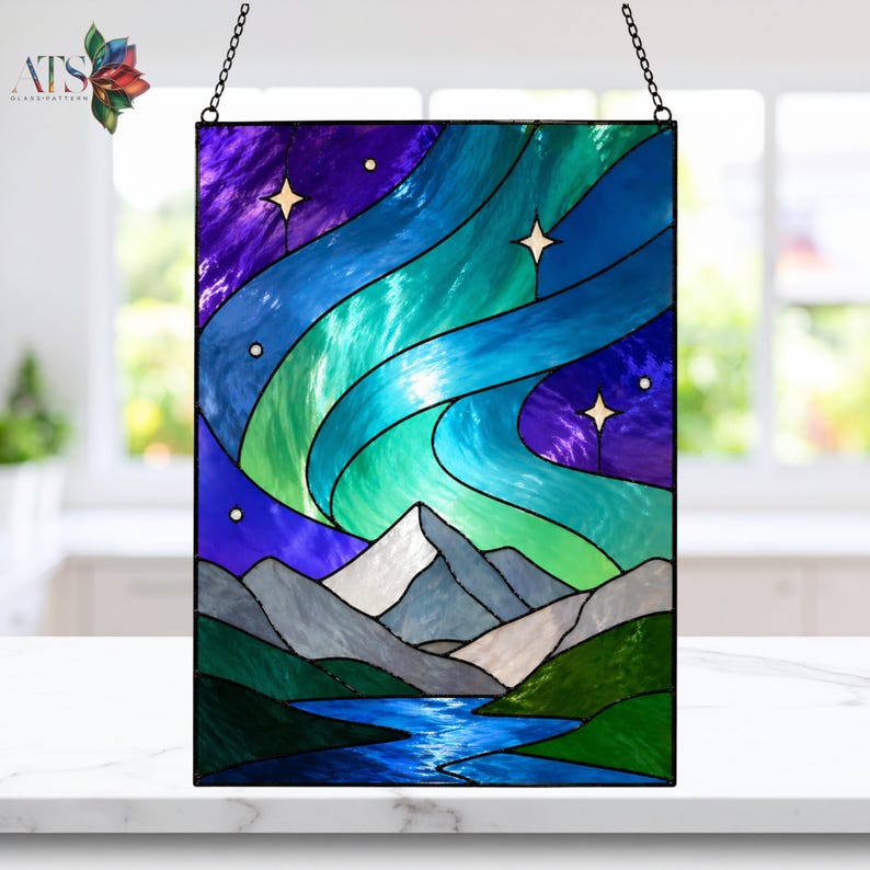 Op de afbeelding: Rechthoekig glas-in-loodpaneel met het noorderlicht boven een bergketen en rivier. Het kunstwerk gebruikt blauw, groen en paars, met witte sterren en bergtoppen. Het paneel hangt aan een ketting. De afmetingen zijn in centimeters.
