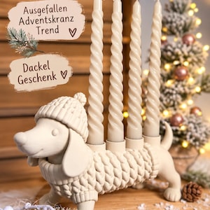 Könnte beinhalten: Ein cremefarbener Kerzenhalter in Dackelform, der einen Strickpullover und eine passende Mütze trägt. Die Figur hat vier zylindrische Öffnungen auf dem Rücken, in denen jeweils eine lange, cremeweiße gedrehte Stabkerze steckt. Text: Kerzenhalter Adventskranz, Ausgefallen Adventskranz Trend, Dackel Geschenk.