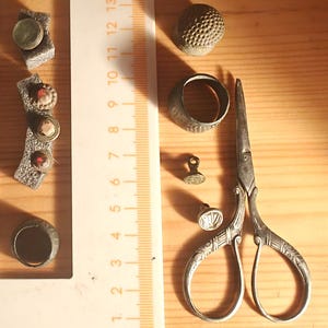 Peut inclure: Ensemble d'outils et d'accessoires de couture anciens, comprenant un dé à coudre, une bague, des ciseaux et divers boutons décoratifs. Les ciseaux mesurent environ 11,4 cm de long. Les articles sont disposés sur une surface en bois.