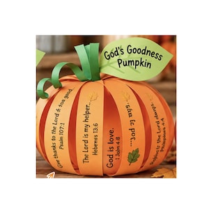 May include: A paper craft pumpkin made of orange strips with printed Bible verses and a green leaf cutout at the top. The leaf features the text God's Goodness Pumpkin. The strips include text such as Give thanks to the Lord, The Lord is my helper, God is love, and Rejoice in the Lord always.