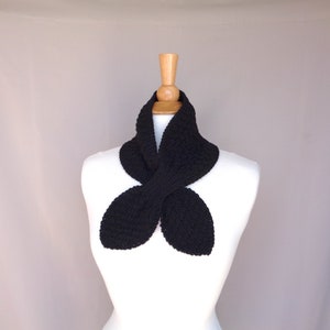 May include: A black knitted scarf with a unique butterfly shape. The scarf is displayed on a white mannequin.