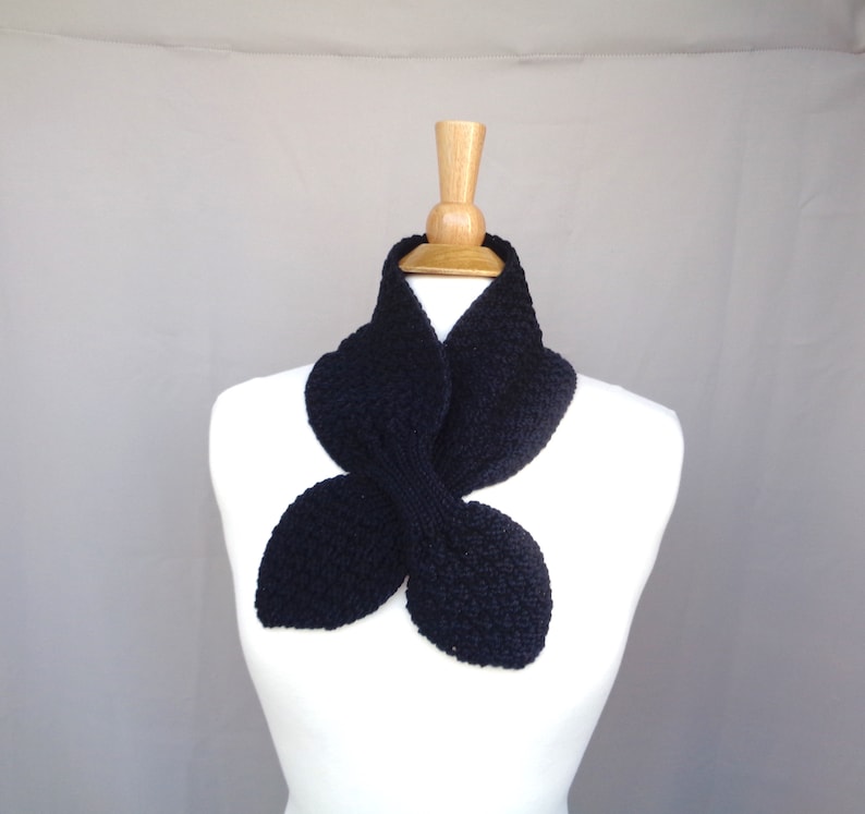 May include: A black knitted infinity scarf with a unique butterfly shape. The scarf is made from a soft, textured yarn and is perfect for adding a touch of style to any outfit.