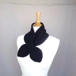 May include: A black knitted scarf with a unique butterfly shape. The scarf is displayed on a white mannequin.
