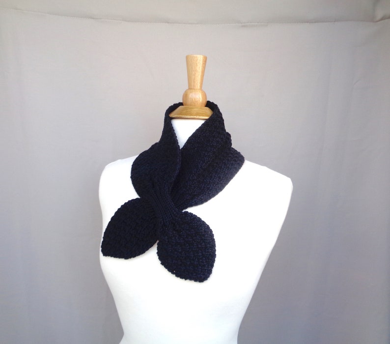 May include: A black knitted scarf with a unique butterfly shape. The scarf is displayed on a white mannequin.