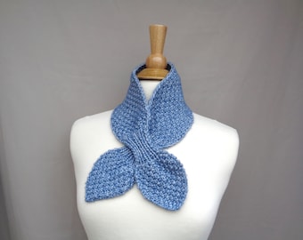 May include: A blue knitted scarf with a unique, folded design. The scarf is displayed on a white mannequin.