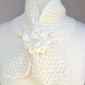 May include: A white crocheted scarf with a large flower detail. The scarf is made of a soft, delicate yarn and has a simple, elegant design.