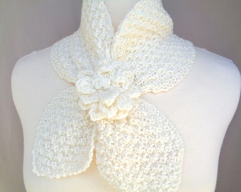 May include: A white crocheted scarf with a large flower detail. The scarf is made from a soft, delicate yarn and has a simple, elegant design.