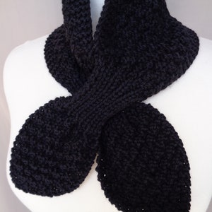 May include: A black knitted scarf with a unique, twisted design. The scarf is made from soft, chunky yarn and has a relaxed, casual look.
