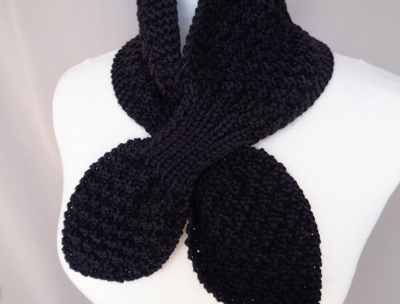 May include: A black knitted scarf with a unique, twisted design. The scarf is made from soft, chunky yarn and has a relaxed, casual look.