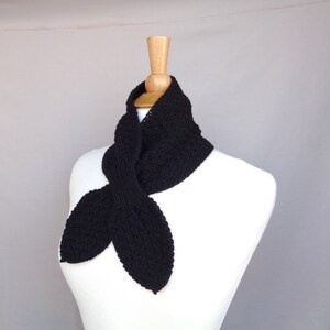 May include: A black knitted scarf with a pointed end, displayed on a white mannequin.