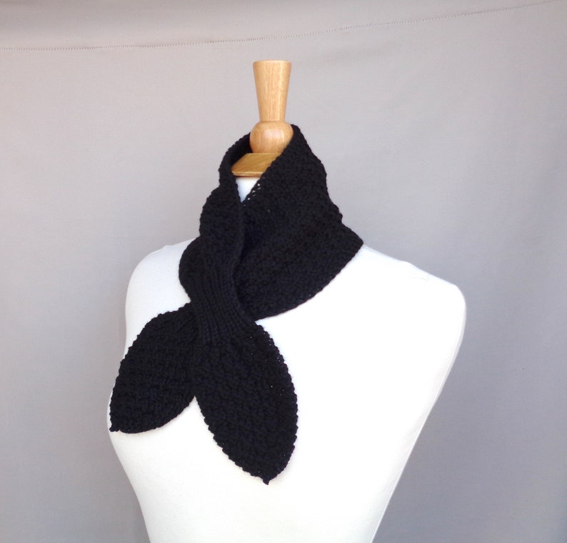 May include: A black knitted scarf with a pointed end, displayed on a white mannequin.