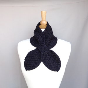 May include: A black knitted neck warmer with a unique, folded design. The warmer is displayed on a white mannequin.