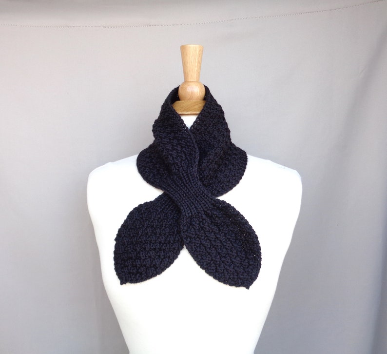 May include: A black knitted neck warmer with a unique, folded design. The warmer is displayed on a white mannequin.